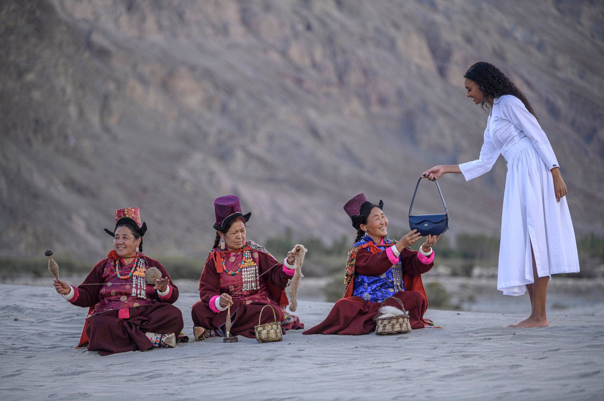 Woman in a white dress giving Linearity bag as gift to four women in traditional attire on a desert landscape.