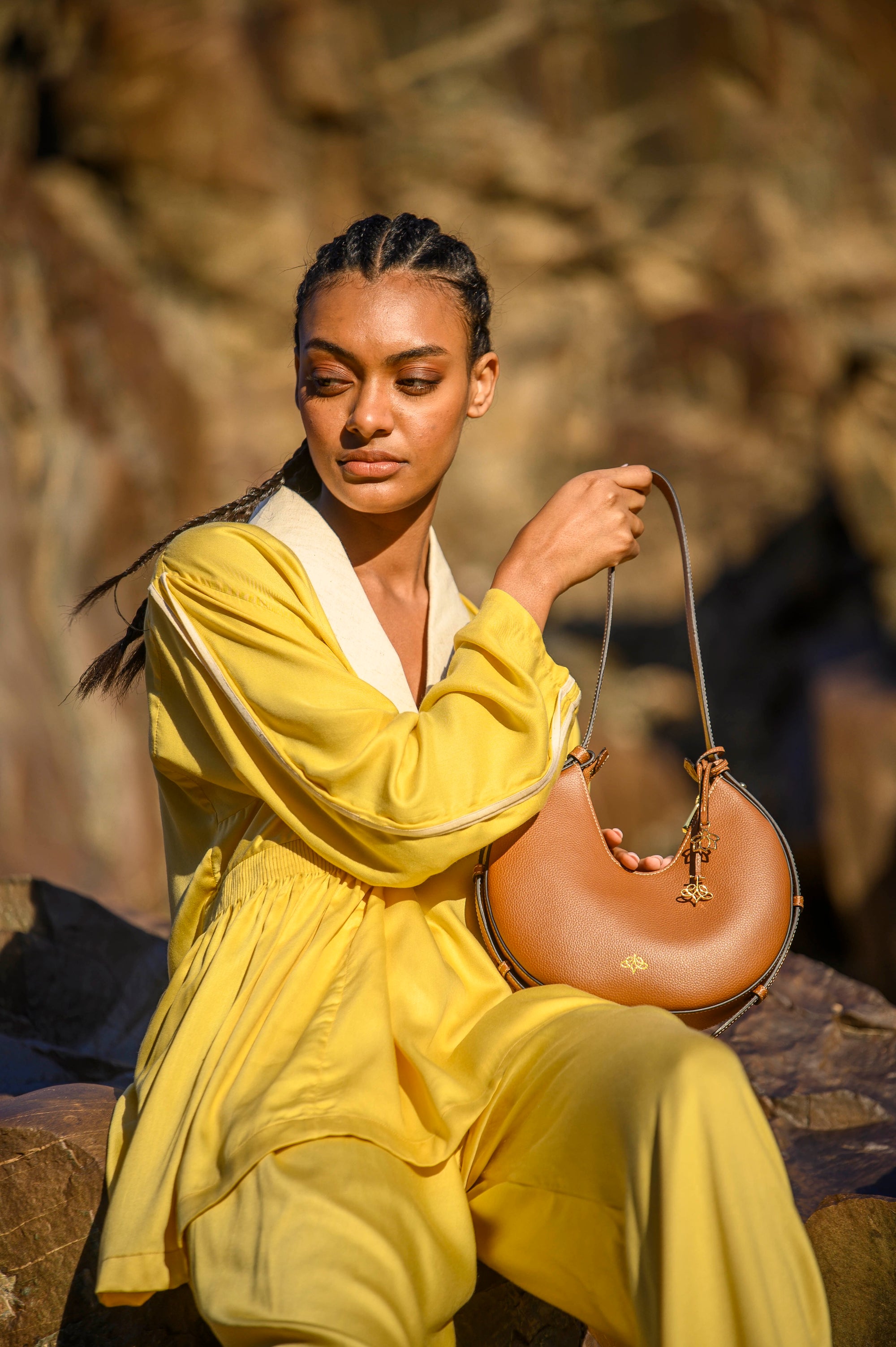 Woman in yellow outfit holding a brown linearity handbag against a blurred natural background