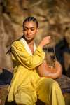 Woman in yellow outfit holding a brown linearity handbag against a blurred natural background