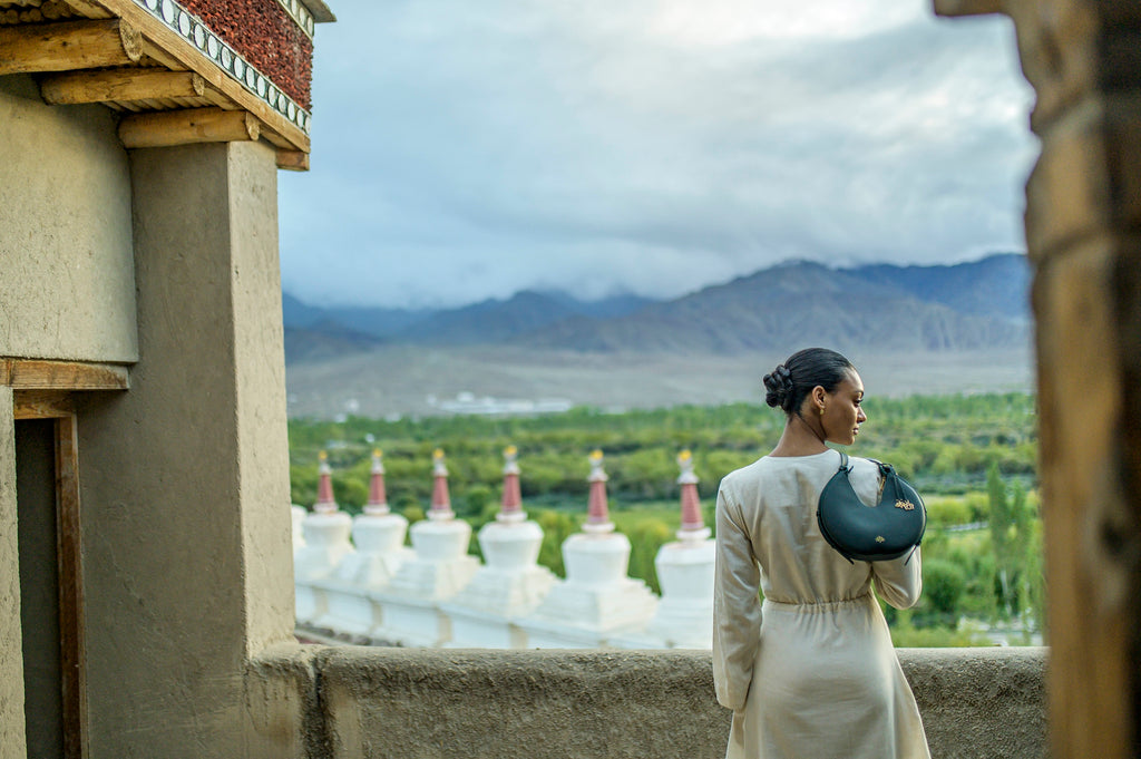 Woman standing on a rooftop with a green linearity bag in a scenic view of mountains and greenery.