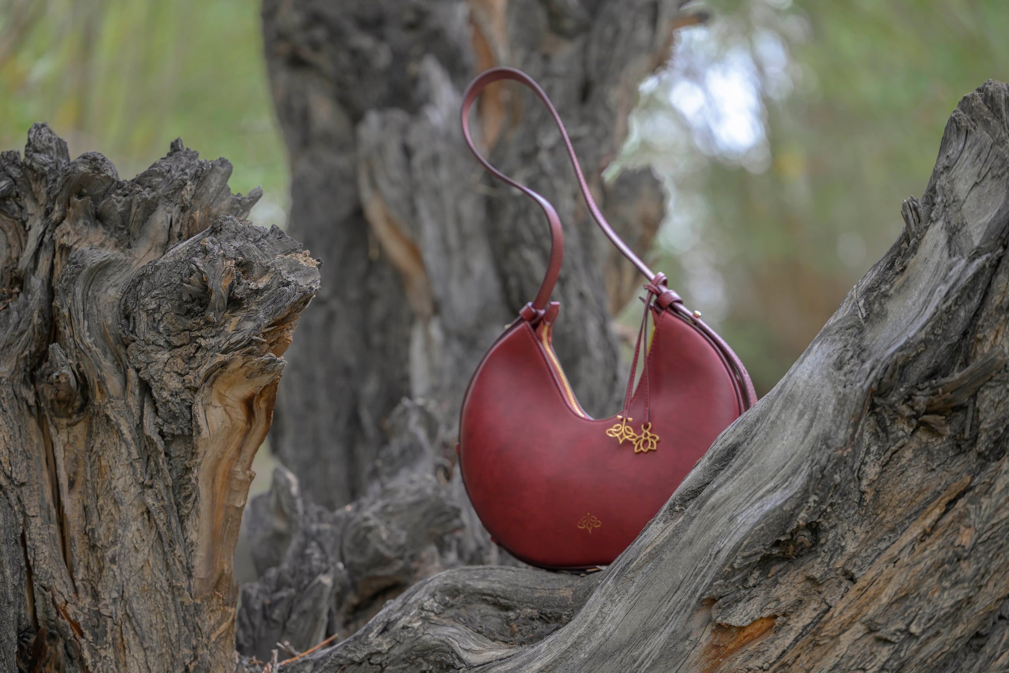 Bordeaux linearity handbag with gold emblem on a textured tree branch