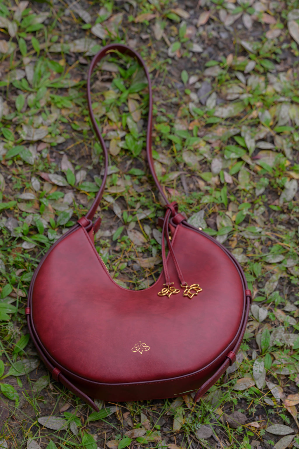 Maroon handbag with linearity logo on a green leafy background