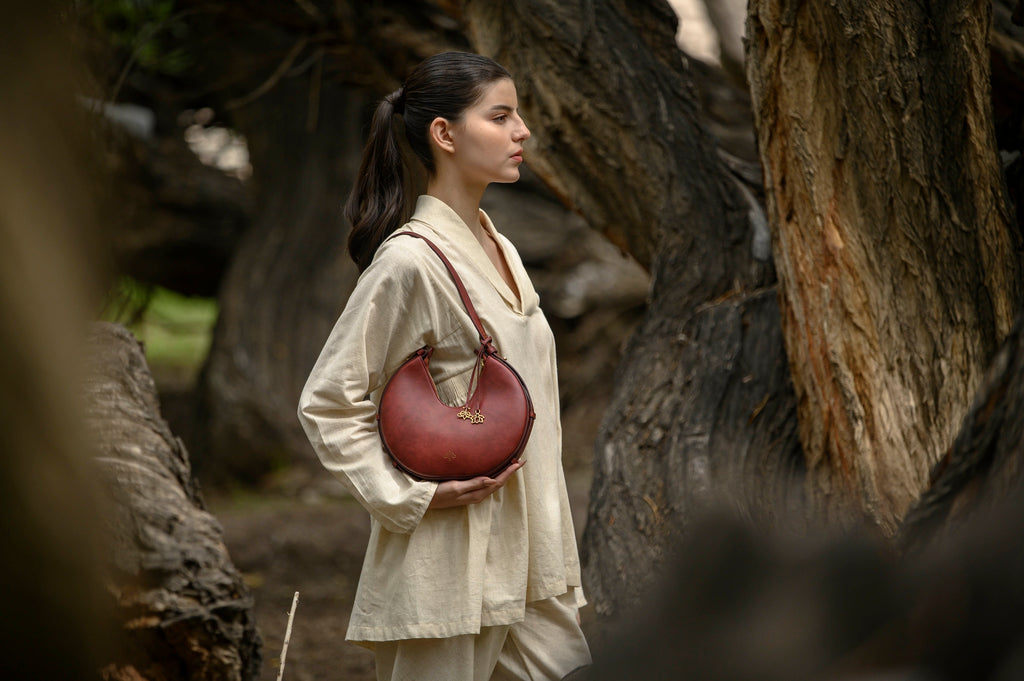 Woman holding a bordeaux linearity handbag in a natural setting with trees.
