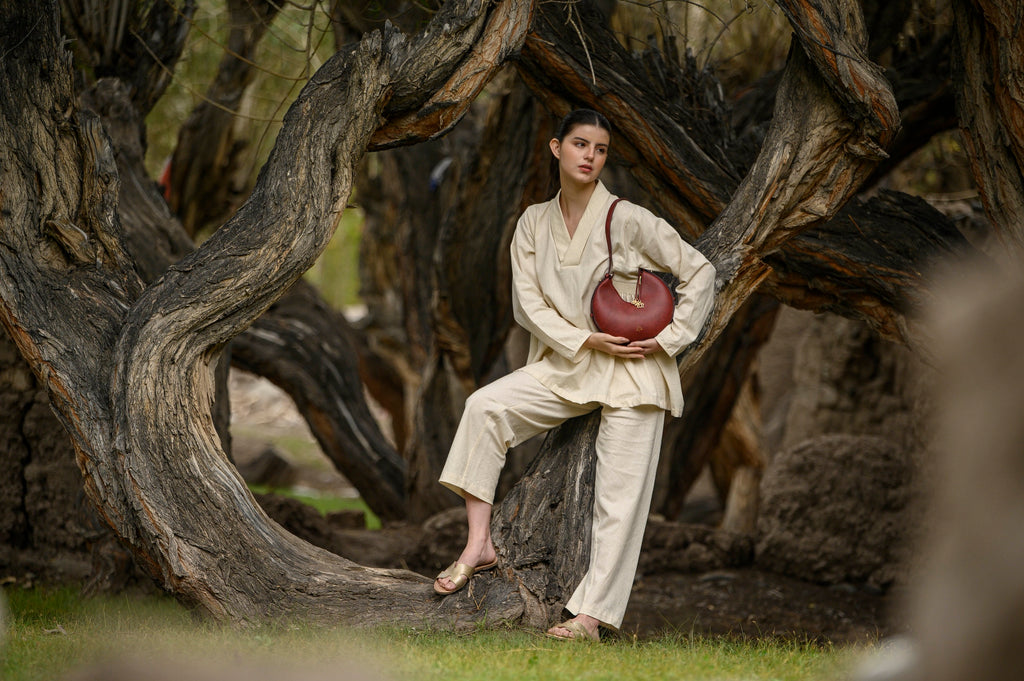Person in a beige outfit sitting under a large tree holding a bordeaux linearity bag.