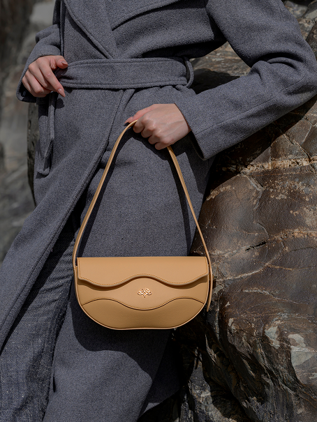 Model holding the golden sand handbag against a stone wall