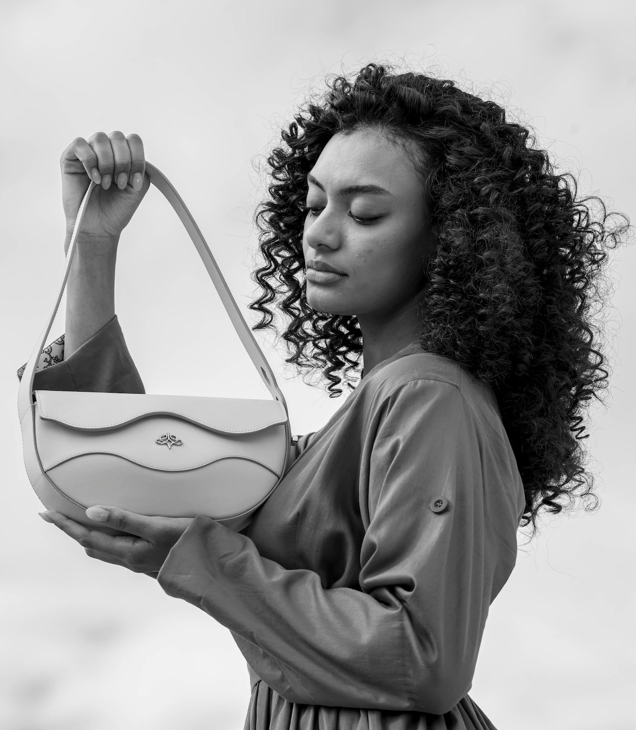 Woman holding a light-colored Linearity handbag against a plain background