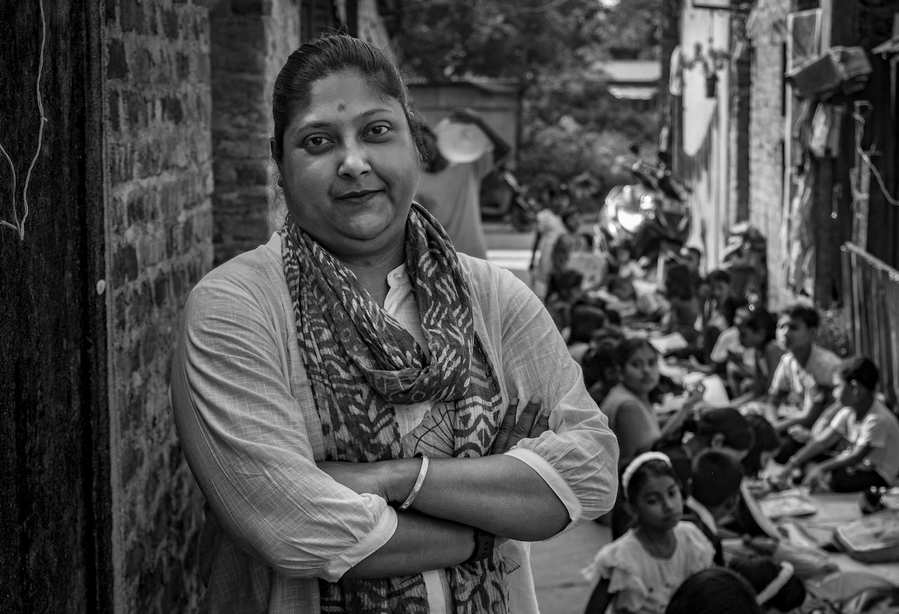 Black and white photo of Jayee standing in an outdoor setting with kids around her.