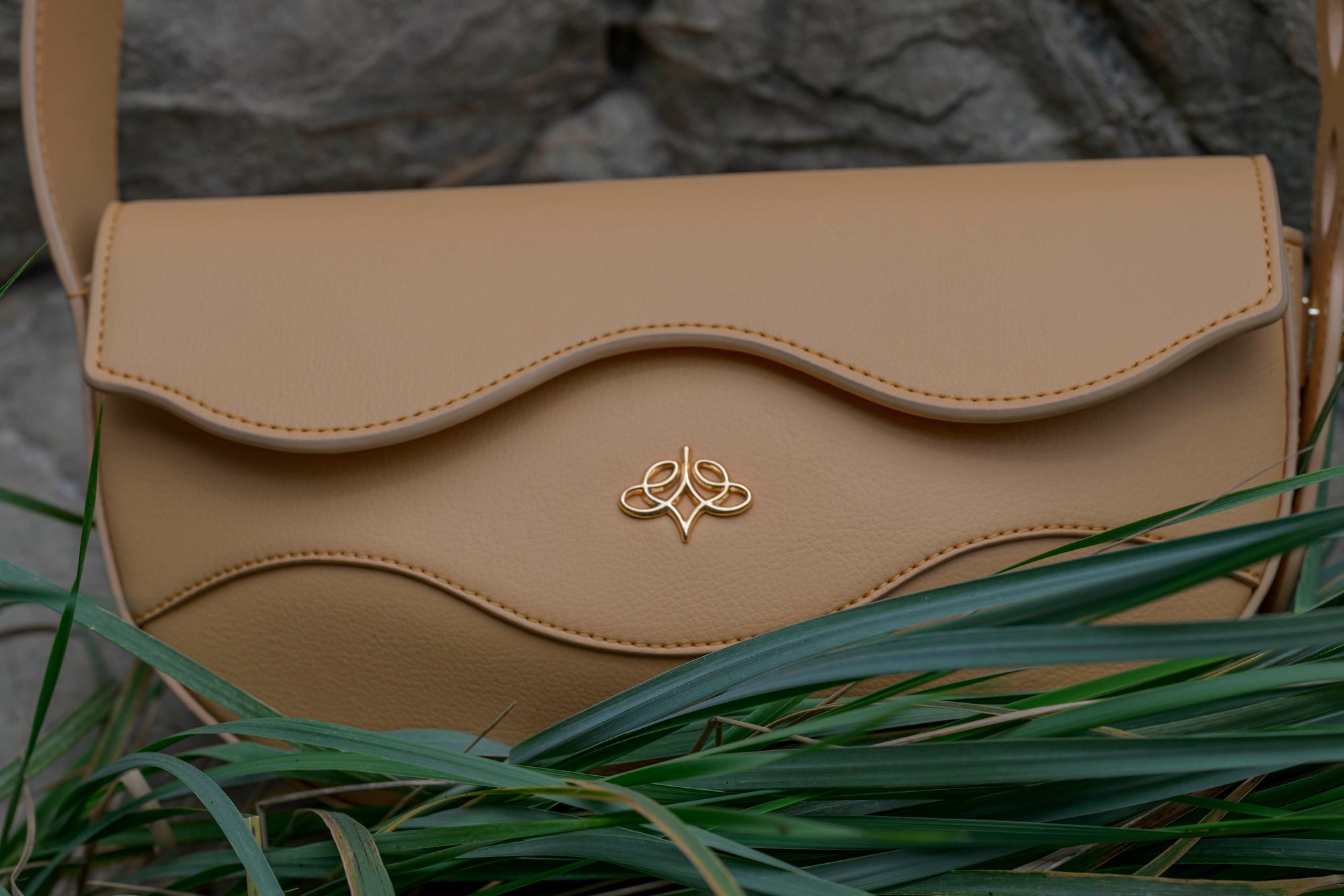 Beige handbag with Linearity logo on grass and stone background