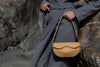 Person holding a beige Linearity handbag with a dark coat against a rocky background