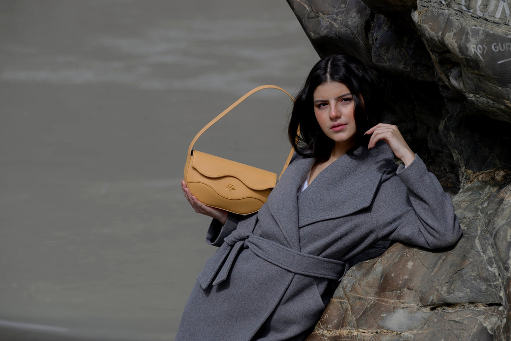 Woman holding a brown linearity handbag against a stone wall