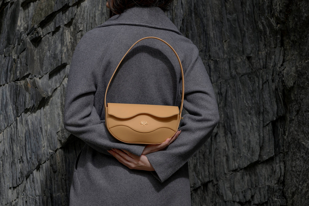 Person holding a beige linearity handbag against a textured wall