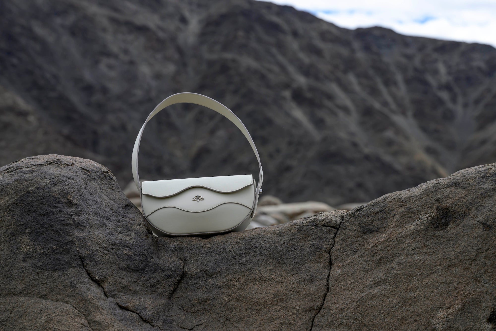 Ascot Grey linearity handbag on a rocky surface with a mountainous background