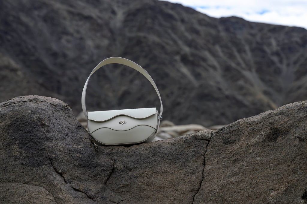 Ascot Grey linearity handbag on a rocky surface with a mountainous background