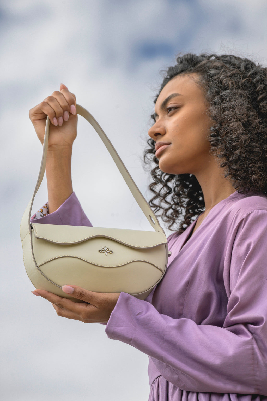 Woman holding a Linearity handbag against a cloudy sky