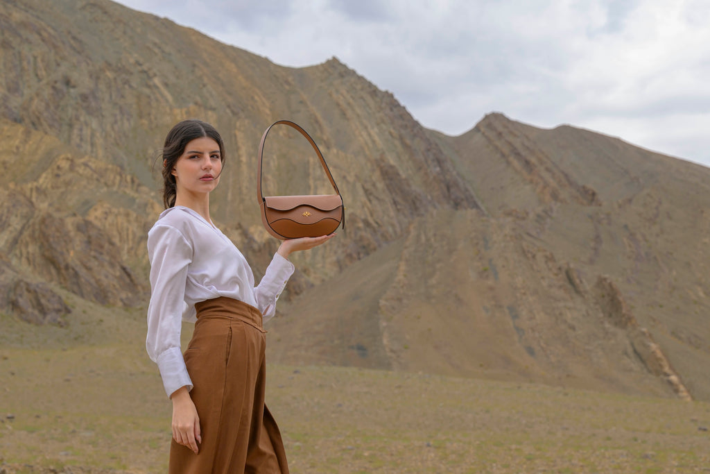 Woman holding a brown linearity handbag in a mountainous landscape