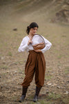 Woman in a white blouse and brown pants holding a brown linearity bag in a desert-like setting