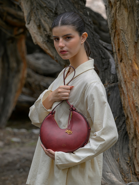 Woman holding the Linearity burgundy handbag with a gold tag in a natural setting